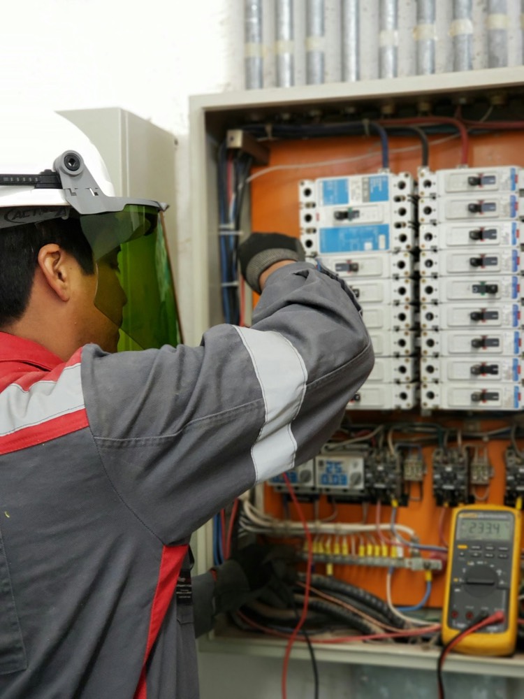 Técnico com proteção facial testando um quadro elétrico